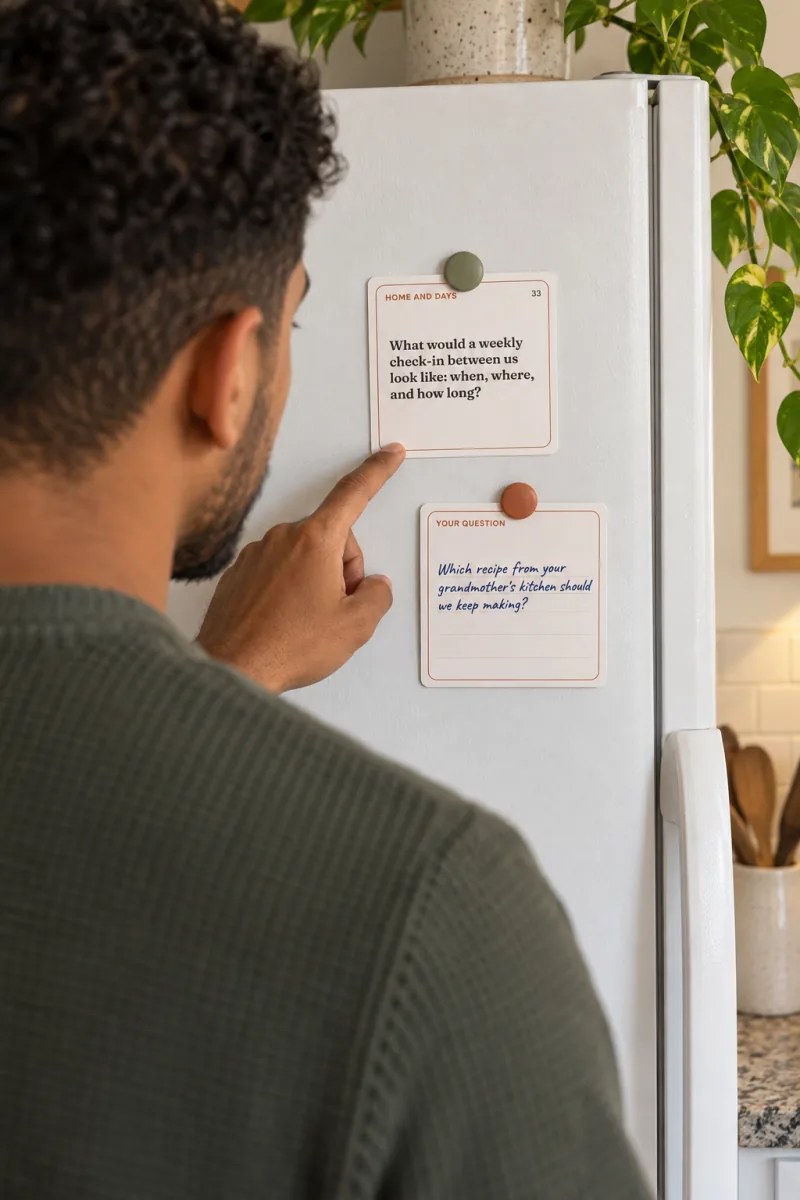 A man points at conversation card 33 held by a magnet on a white fridge, a handwritten card of his own below it
