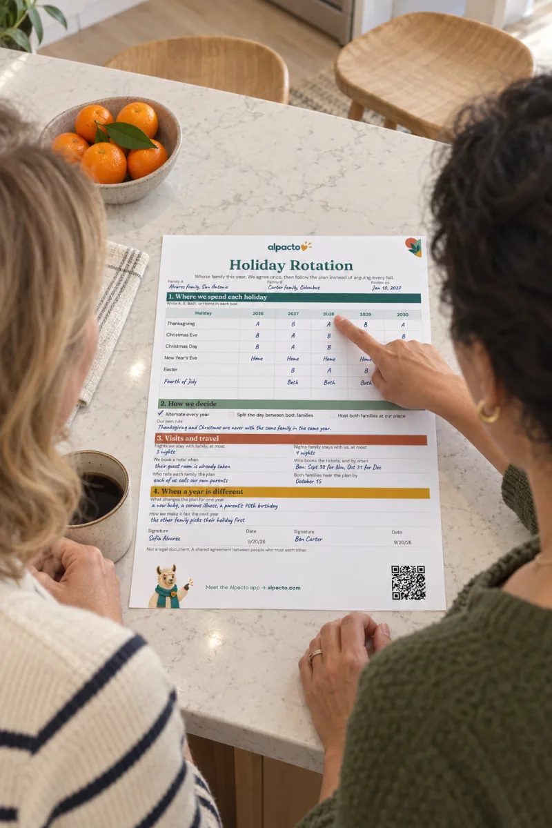 Two women at a kitchen island, one points at the 2028 column of the filled-in holiday rotation sheet