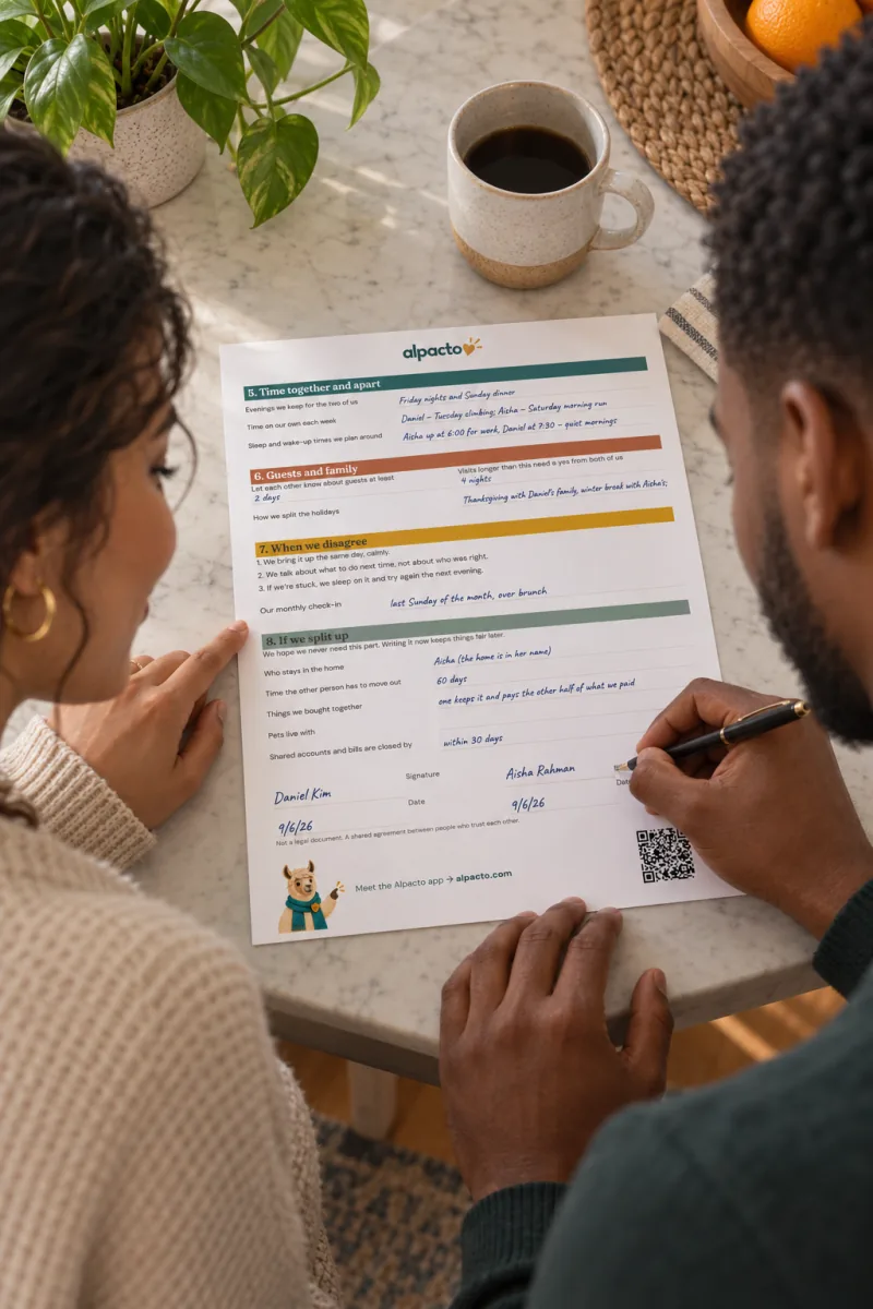 A couple at a kitchen table signing page 2 of the living together agreement